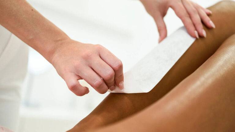 Épilation des jambes d'une femme de carnation matte par une esthéticienne