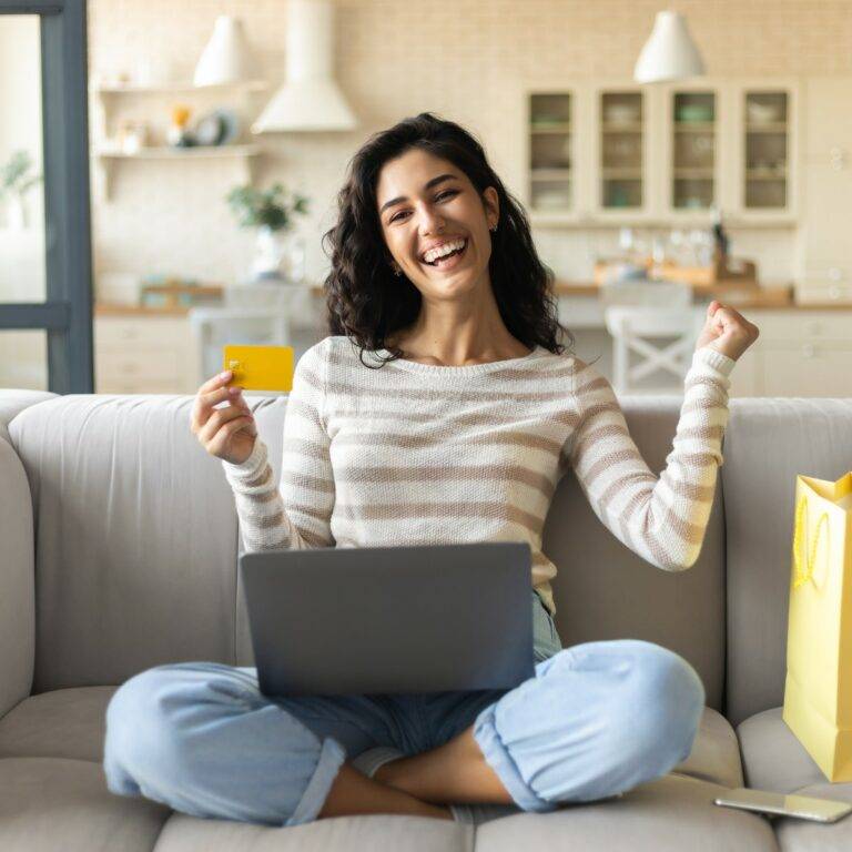 Femme souriante tenant une carte bancaire devant son ordinateur portable